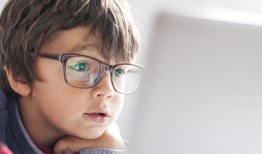 A little boy wearing glasses looking at a computer