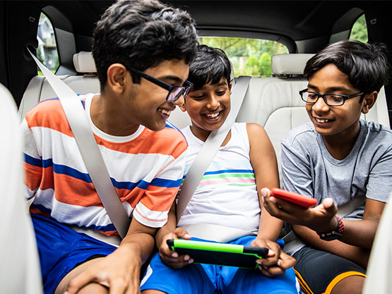 Three boys in the backseat of a car smiling and looking at a phone