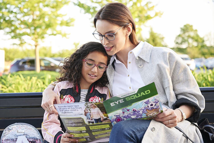 mother and daughter with glasses reading an eye magazine outside on bench