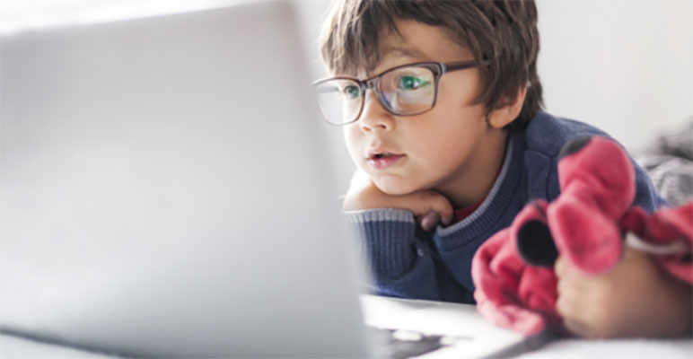 boy with glasses laying down looking at a laptop