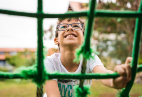 A boy with glasses climbing up a playground net