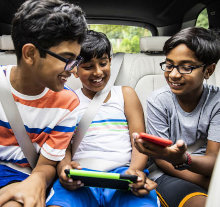 A group of three boys in a car looking at a phone and tablet